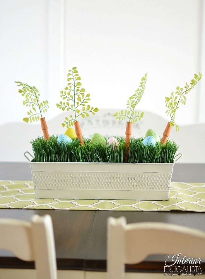 An upcycled Easter centerpiece box with faux wheatgrass, chair spindle carrots, and DIY speckled eggs for a fun budget Easter table decoration idea.