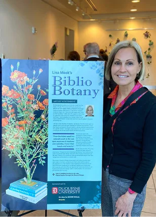 smiling woman in black cardigan and bright floral blouse standing next to sign explaining BiblioBotany museum exhibit
