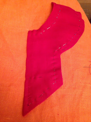 A screaming red keyhole collar piece, pinned in half and seamed at the lower point, laid out on bright-orange fabric.