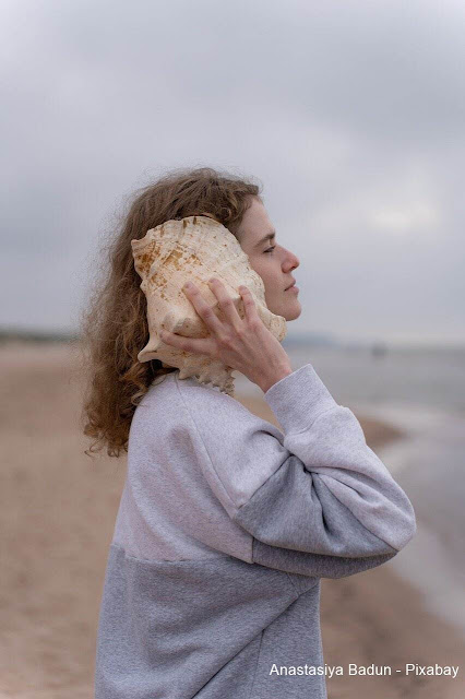 Mulher na praia ouvindo um búzio.