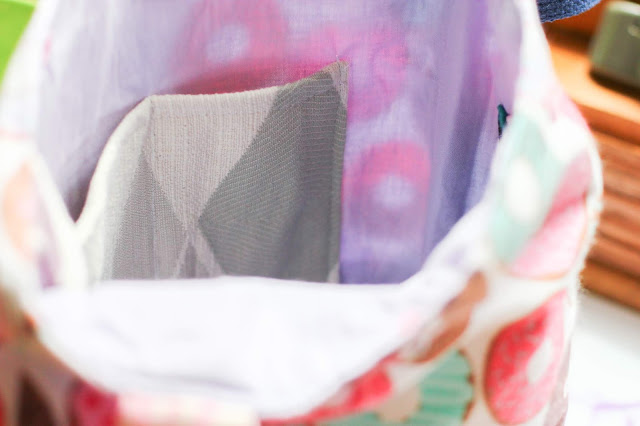 Lilac interior of a donut print project bag with focus on a shades of grey and ecru largescle argyle patterned fabric used as a dual pocket.