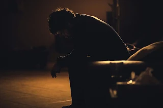 A man sat hunched in a chair, showing his insecurities, worries and vulnerability.