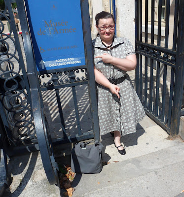 Image shows a person pointing with one hand to a sign which reads "Musee de L'Armee Access for Diseabled Persons," and pointing with the other hand to the stairway the sign refers to.