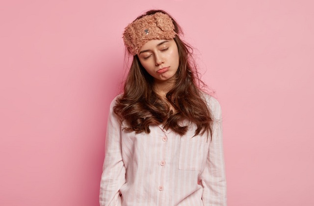 Tired woman in pajamas with eye mask looking tired and pouting