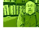 This is a picture of an older man with a thick beard sitting in front of a full bookcase. This picture is tinted green, so no other colors are present.