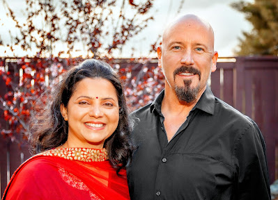 Nidhi in red sari, David in black shirt, smiling.