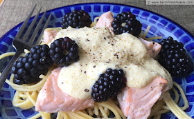 image of a blue plate of spaghetti topped with flakes of salmon, fresh blackberries, and a lemon cream sauce