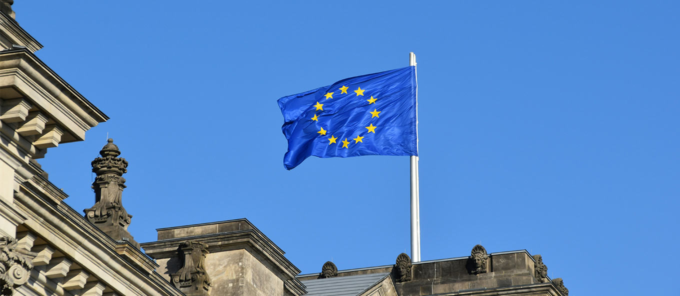 A close-up photo taken of the European Union flag blowing in the wind on top of a building.