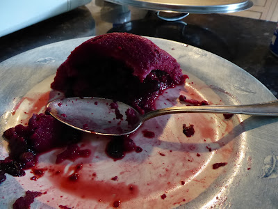 A dark pink pudding, partly eaten, on a plate with a serving spoon.