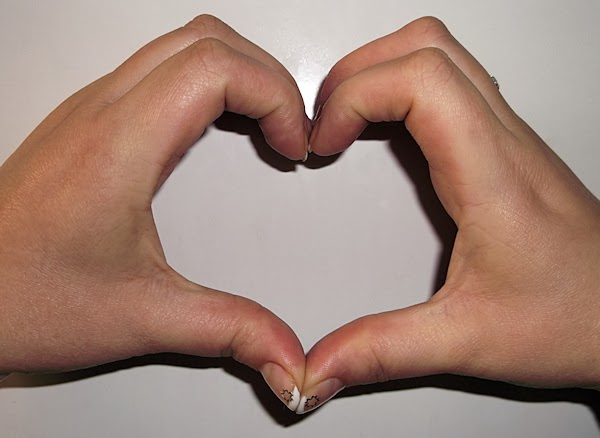 Serce na białym tle z kobiecych dłoni z końcówkami paznokci pomalowanymi na biało i naklejonymi gwiazdkami
