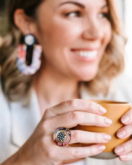 smiling woman holding mug wearing colorful, large earrings and ring