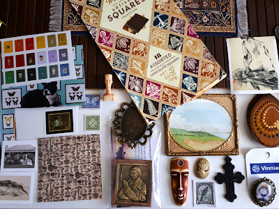 A range ofone-twelfth-sized items of miniature art set out neatly on top of a wooden floor and a turkish rug..