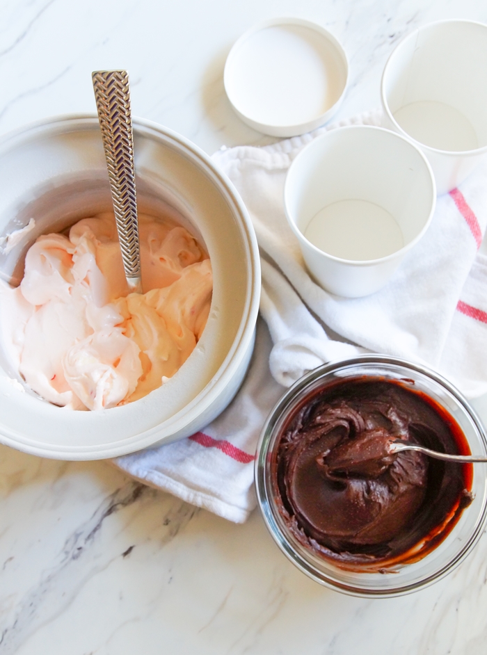 pink ice cream in ice cream freezer bowl with separate bowl of chocolate sauce