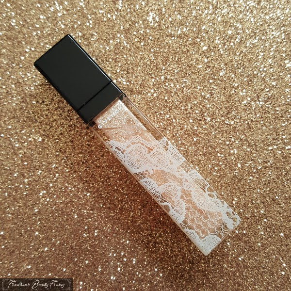gold sparkling lipgloss with black lid and white lace design on bottle on glitter background