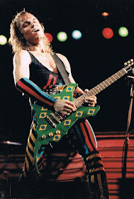 Foto de Matthias Jabs no palco do primeiro Rock in Rio com a icônica guitarra no formato do logo do festival, verde e com bandeirinhas do Brasil.