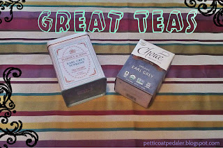 Striped fabric background or mostly yellows and burgundies.  Two boxes of tea sitting on top of the fabric with the Text, "Great teas," over the image.  