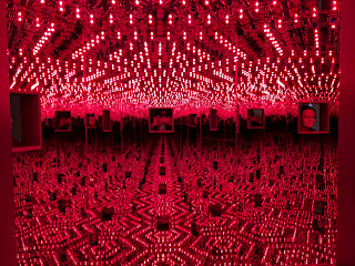 This is a photo of a Yayoi Kusama light installation. There are portals that viewers can look in through. There are mirrors that reflect the lights creating a sense of dimension and infinity.