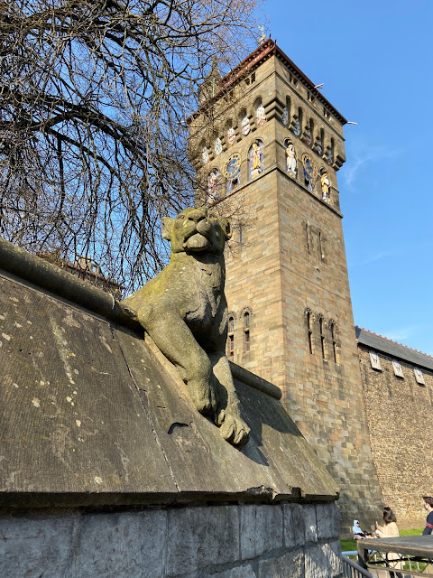 A stone lioness on the Animal Wall, Cardiff, with part of the castle in the background