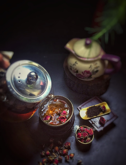 "A teapot surrounded by dried rose petals and loose tea leaves, symbolizing the process of crafting Chinese Rose Tea."