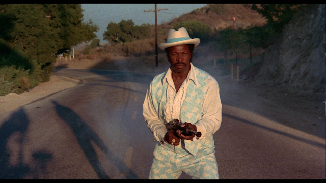 Dolemite shooting a gun while the camera crew's shadow is in the background