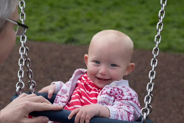 A smiling baby on a baby swing in a pink and white striped dress