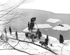 A photograph of a film crew working at a snowy river's edge.