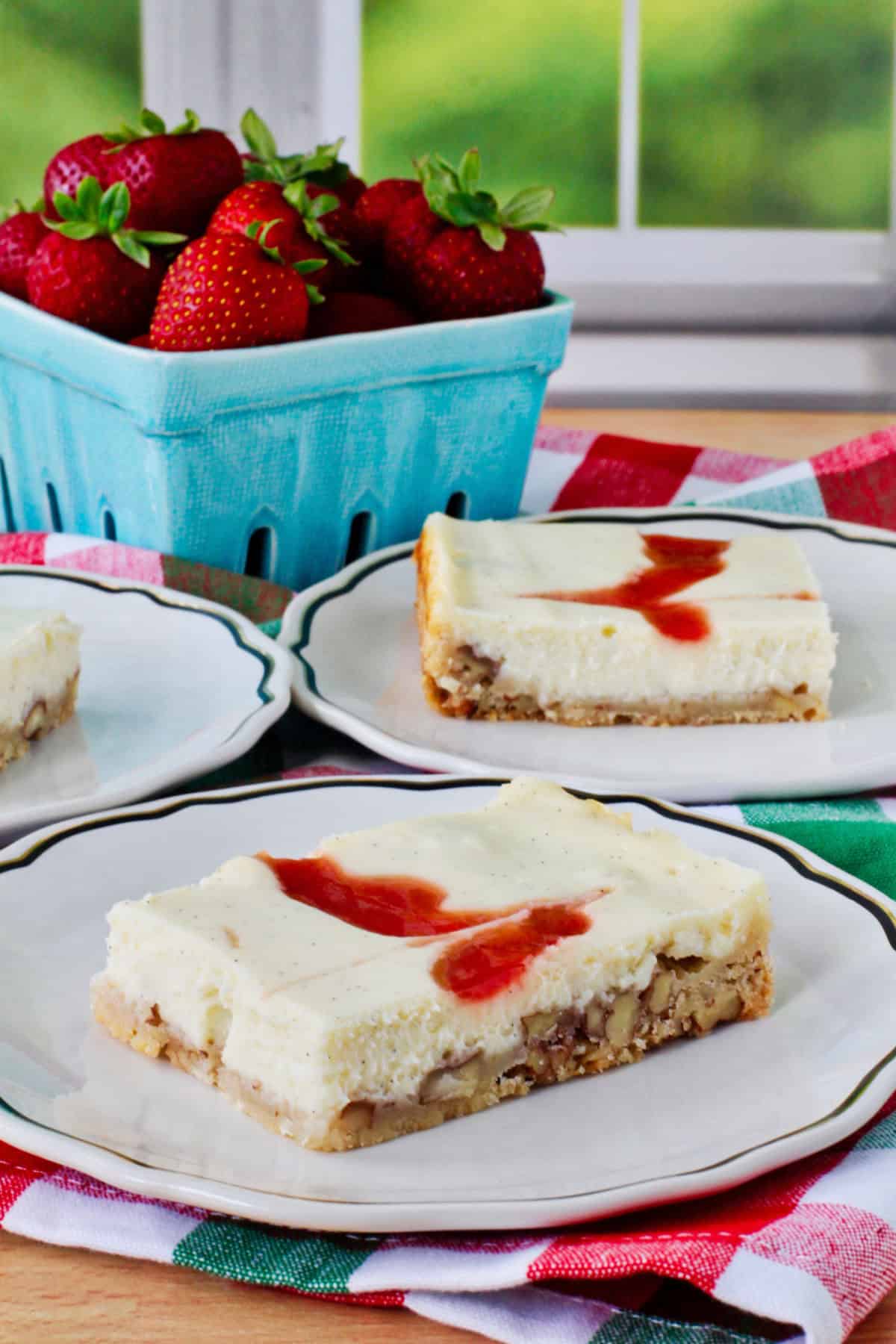 Strawberry Cheesecake Bars on plates with strawberries in the background.