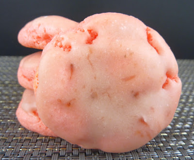 Strawberry-pink strawberry cake mix cookies, topped with a strawberry glaze, photographed on a dark grey mat