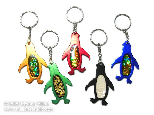 Five anodized penguin keychains filled with resin, iridescent mylar, gold leaf and glitter.