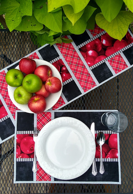 white plate and table setting on red, black and grey placemats with apple print fabric