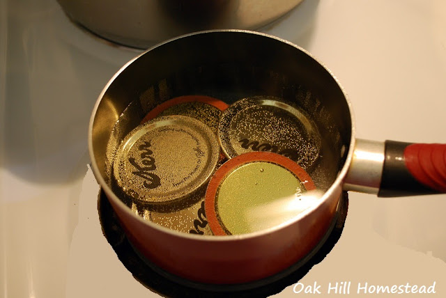 A red saucepan holding canning lids in water.