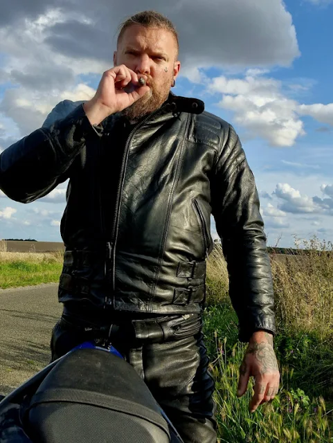 From these outstanding next to motorcycle bearded biker smokes cigar blue skies in the background what
