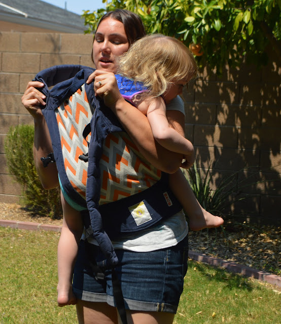 The wearer is seen pulling the panel of the carrier up over her baby's back