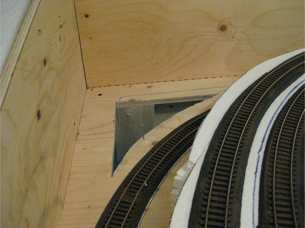 A triangular hole cut through the benchwork next to the model railroad track in the future tunnel