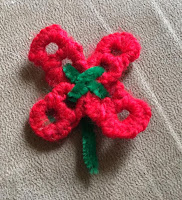 Red poppy with a green center made from pop tabs, yarn, and a green pipe cleaner.