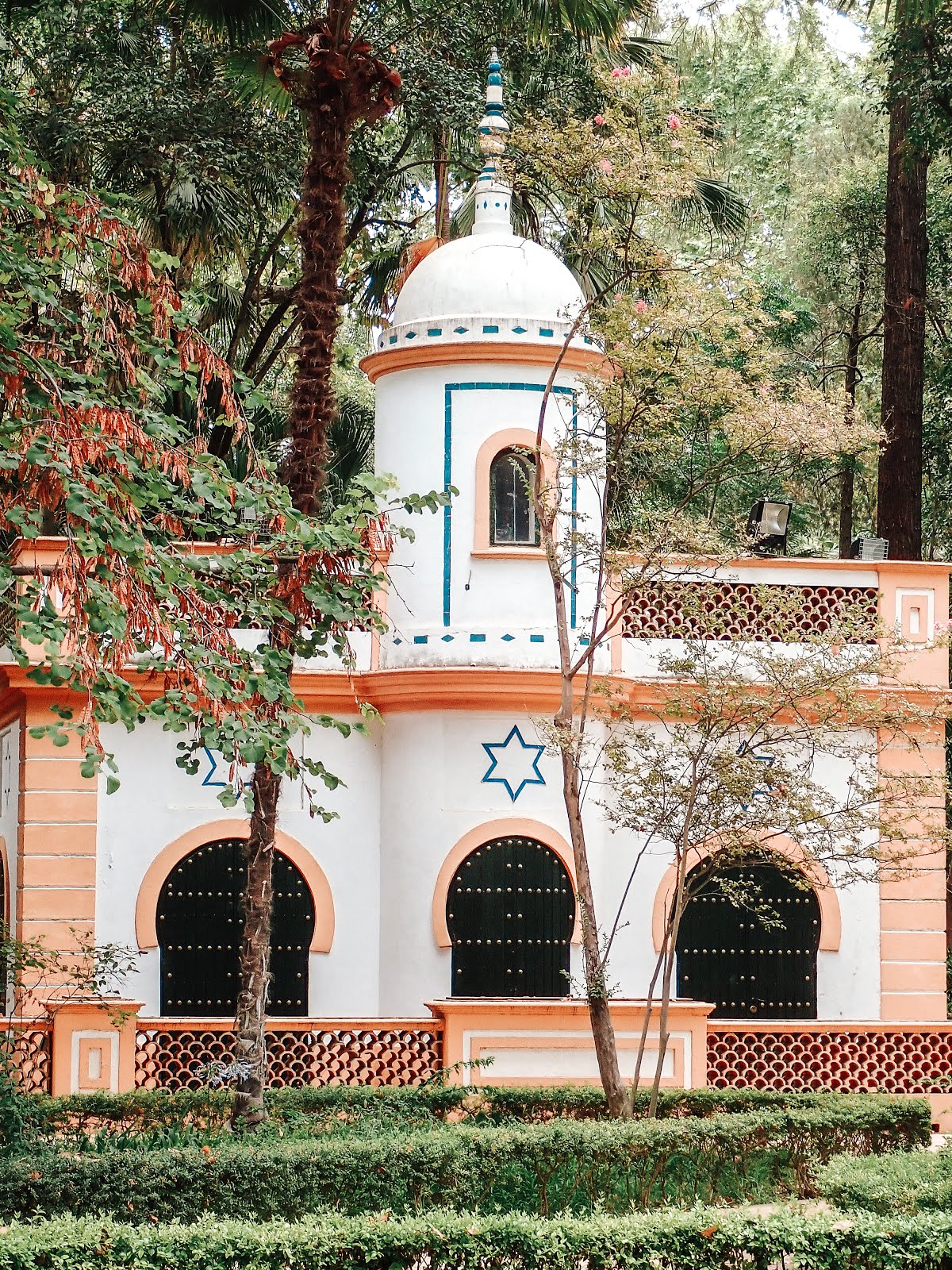 un bâtiment du parc maria luisa de séville de style architectural islamique de couleur blanche avec des liserés orange et bleu et une étoile à 6 branches