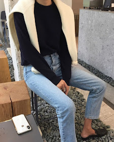 Effortless spring outfit idea from deathbyelocutionblog with a cream sweater over the shoulder, basic black sweater, straight-leg jeans, and mule flats loafers