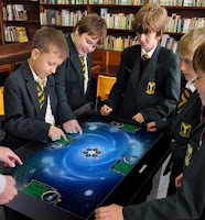 A group of school children standing around a digital table learning chemistry