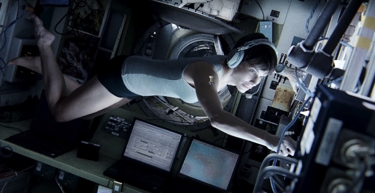 Astronaut in skivvies floating inside space station with headphones on and working at control board