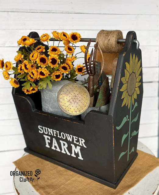 Photo of a large wooden tote painted with black chalk paint, stenciled with Sunflower Farm Stencil, and filled with vintage garden decor.