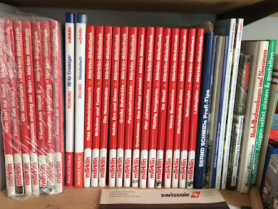 Märklin-Bibliothek die roten Buchrücken mit ihren Titel stehen im Regal aufgereiht. Links sind noch einige in Plastikeingewickelt. Auch andere Modellbahnbücher finden sich.