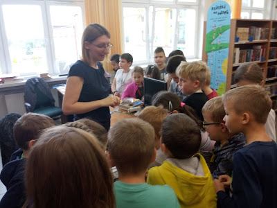 Na zdjęciu bibliotekarz przy ladzie tłumaczy jak zapisać się do biblioteki