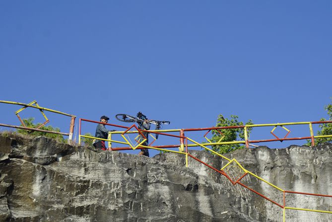 Pesepeda memanggul sepedany ke atas tebing di Bukit Tompak