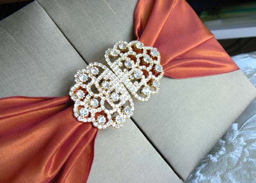 Glimmering crystal brooches delicate satin ribbons and regal silk boxes are