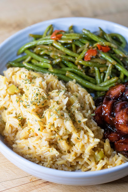 The instant pot rice pilaf on a plate with green beans and bbq smoked sausage.