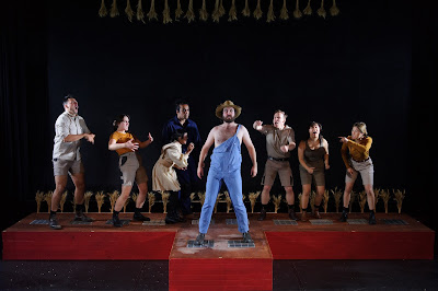 7 performers in farm clothes looking at a farmer