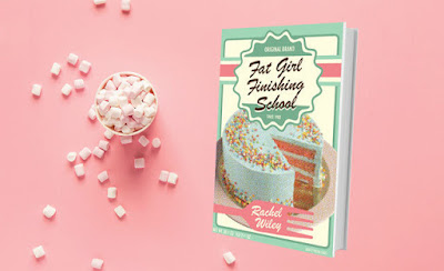 A book sits next to a cup overflowing with marshmallows. The book cover is pink and green. It has a cake with a slice cut out of it and a cartoon fork in front of the cake. The text reads 'Fat Girl Finishing School' 'Rachel Wiley'