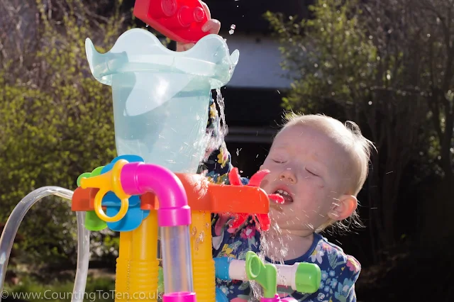 Close up of a toddler trying to pour water into a funnel and getting splashed