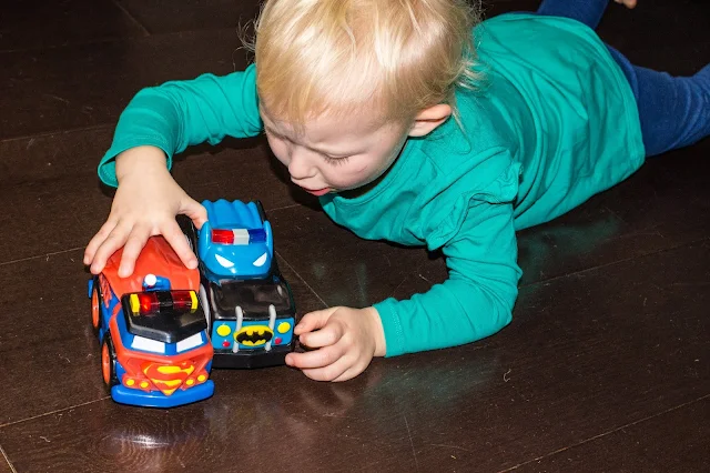 A preschooler on the floor playing with a superman and a batman Herodrives mash machine cars