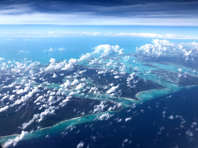 A shot from the air of white fluffy clouds and beautiful water ranging from dark blue to turquoise